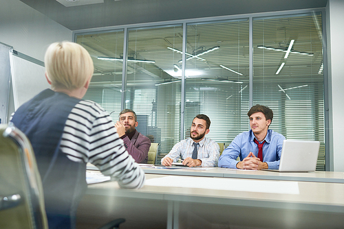 Group of business people sitting at meeting table discussing work in modern office, shot from behind glass wall