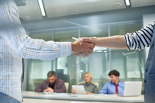 Closeup of two unrecognizable people shaking hands in office against work meeting background