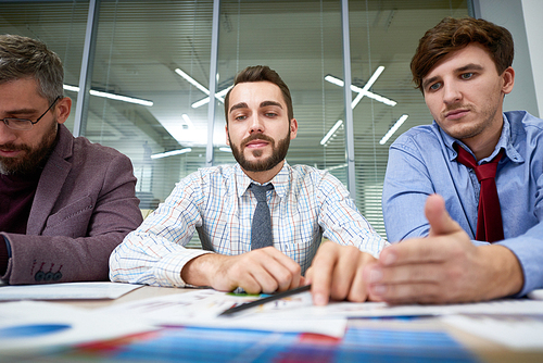 Portrait of three business people sitting at meeting table discussing financial documents in front of them in modern office