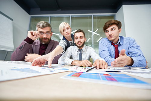 Portrait of three business people sitting at meeting table discussing financial documents  with charts and graphs in front of them in modern office