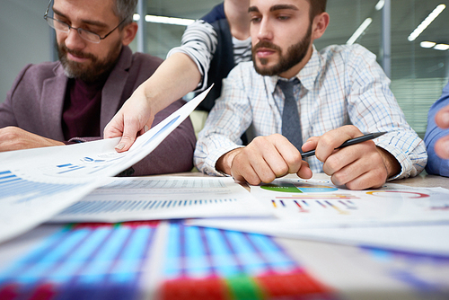 Group of busy business people sitting at table with charts and graphs analyzing financial and marketing statistics for annual report