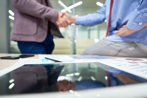 Close-up shot of unrecognizable business partners shaking hands after successful completion of negotiations, messy table surface on foreground