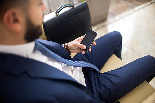 High angle close up of unrecognizable businessman using smartphone waiting in lobby with leather case