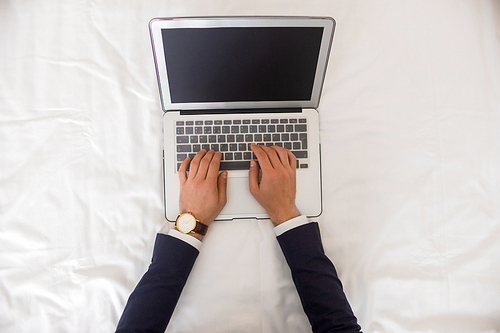 Directly above view of unrecognizable businessman typing on laptop keyboard with computer on bed sheets in hotel