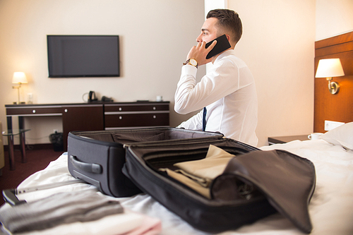 Rear view portrait of successful businessman speaking by phone after arriving to hotel while unpacking luggage