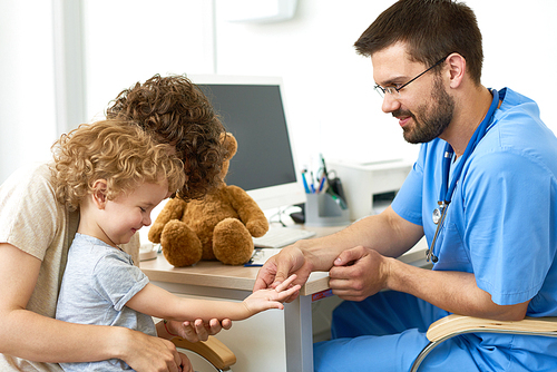 Portrait of little boy in doctors office, pediatrician holding childs hand