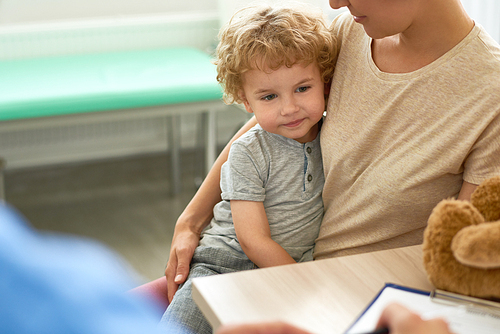 Portrait of adorable little boy  sitting on mothers lap visiting doctor in office , copy space