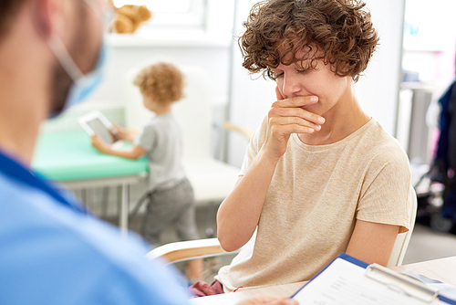 Portrait of distressed young woman talking to doctor in office with little child in background