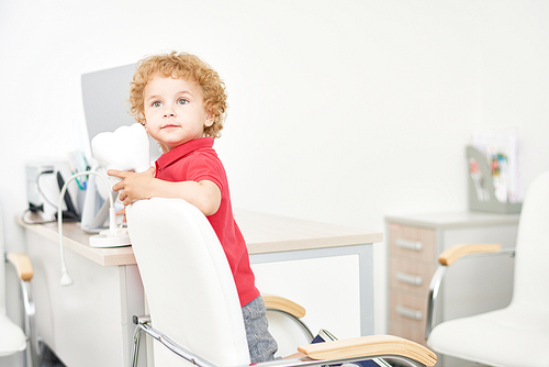 Portrait of cute little boy with blonde curly hair looking away pensively while playing at dental office