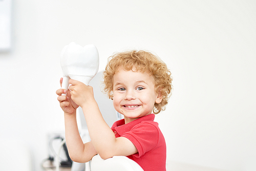 Head and shoulders portrait of cute toddler  while playing with tooth model at dental office, blurred background