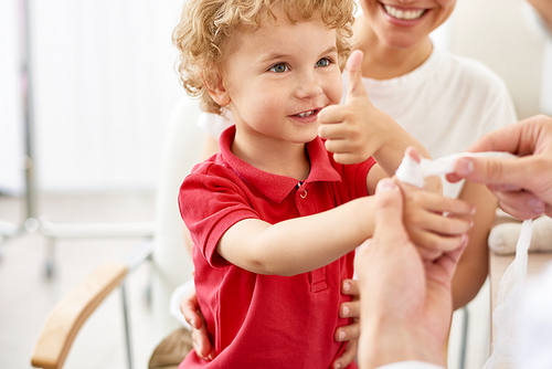 Portrait of adorable curly child showing thumbs up at doctors office during visit with mom