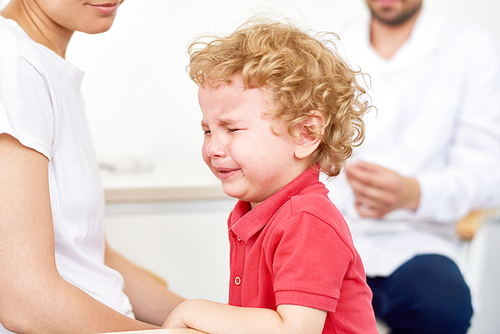 Portrait of scared  little boy hugging mother and crying in doctors office