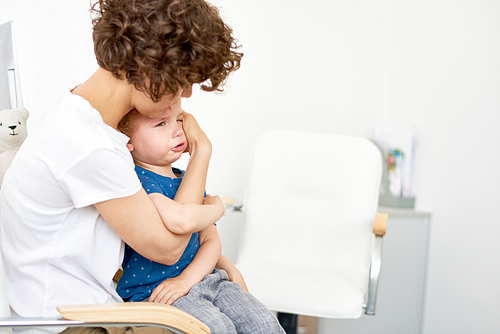 Portrait of young mother trying to calm little boy throwing hysterical tantrum in doctors office, copy space