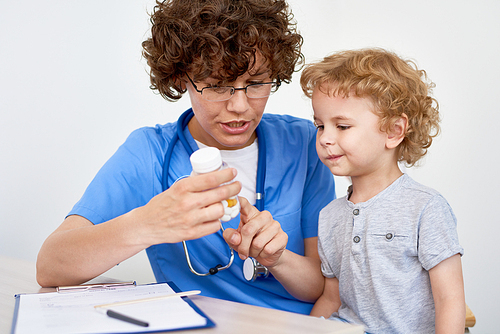 Portrait of young woman doctor showing can of pills and vitamins to adorable little boy