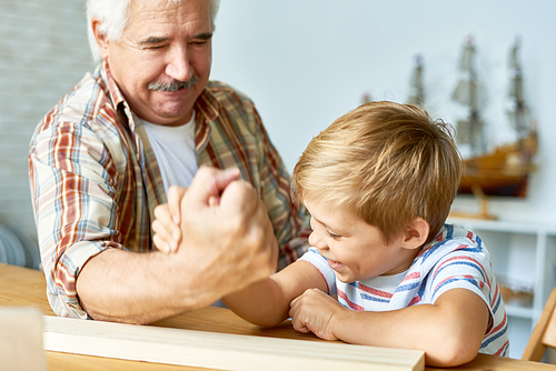 Portrait of white haired senior man armwrestling with  little grandson having fun together ant home