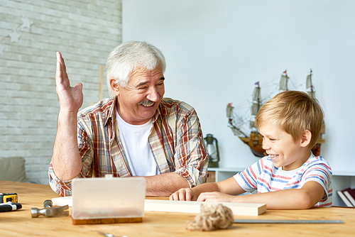 Portrait of happy senior man spending time with his grandson laughing together while teaching him woodwork