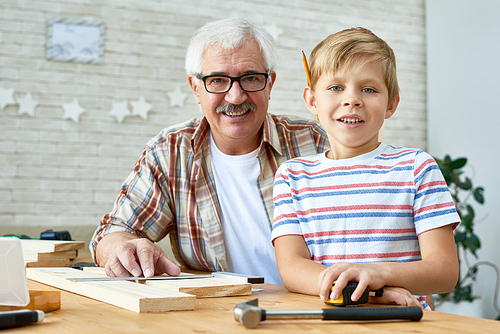 Portrait of grandfather and grandson smiling happily  while building birdhouse together at home