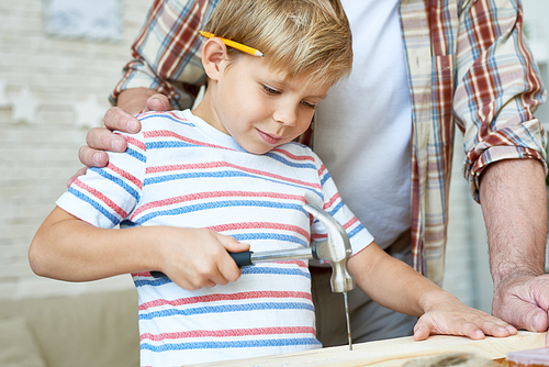 Closeup portrait of senior man helping little boy hammering nails while making wooden model together at home