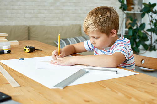 Portrait of cute little boy writing or drawing carefully sitting at desk and doing homework, copy space