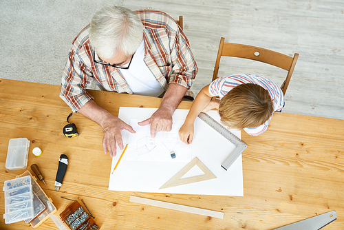 Above view portrait of little boy and granddad sitting together at desk sketching plan of birdhouse for school project