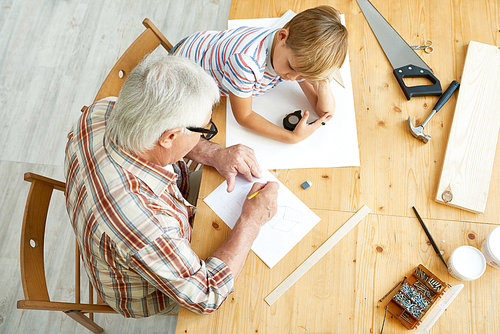 Above view portrait of grandfather and grandson working together at desk drawing sketches of wooden birdhouse