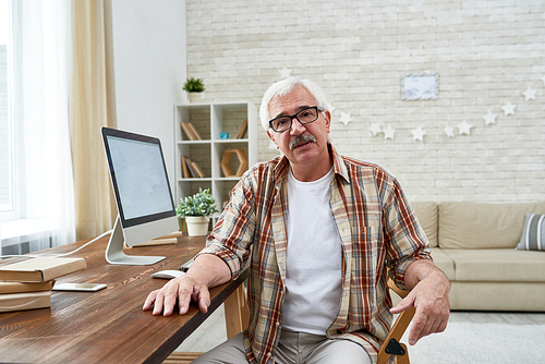 Portrait of white haired senior man wearing glasses sitting at desk with modern computer , copy space