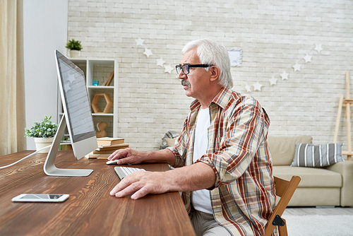 Side view portrait of senior man learning to use modern computer sitting at desk at home