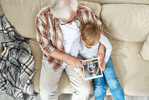 High angle view of grandfather and grandson using digital tablet looking at photos together at home