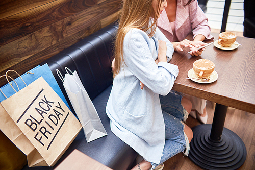 High angle portrait of two beautiful young women in shopping mall chatting and  drinking coffee at cafe table surrounded by paper bags on Black Friday