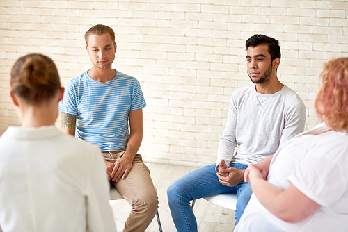 Back view of young psychologist working with group of patients suffering from phobias while sitting in circle at cozy office