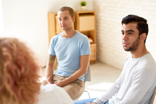 Group of young people sitting in circle sharing mental problems, focus on two modern young men