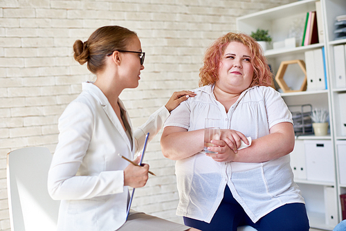 Portrait of  young woman  comforting  crying obese woman during therapy session on mental issues