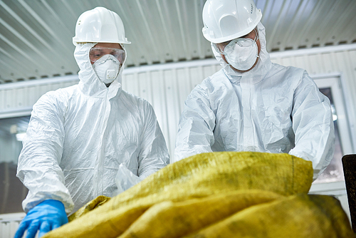 Low angle portrait of two workers  wearing biohazard suits working at waste processing plant sorting recyclable materials on conveyor belt