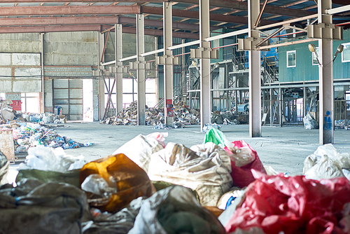 Wide angle image of industrial warehouse of modern waste processing plant, plastic bags of garbage in foreground, copy space
