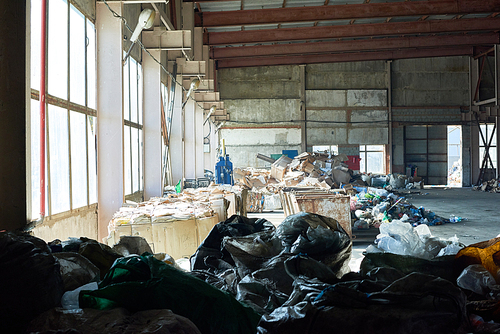 Background image of industrial warehouse of modern waste processing plant, plastic bags of garbage in foreground, copy space
