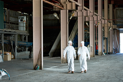 Full length portrait of two workers wearing protective  suits walking across workshop of waste processing plant copy space
