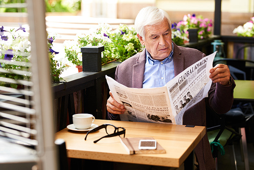 Portrait of modern senior man reading newspaper in cafe outdoors enjoying sunny morning in retirement