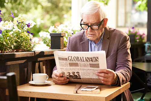 Portrait of senior man reading newspaper at breakfast in cafe outdoors
