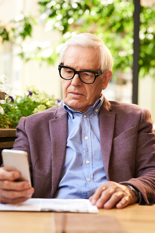 Portrait of modern senior man using smartphone in outdoor cafe, enjoying sunny day