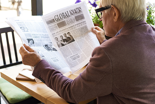 Back view portrait of senior man reading newspaper in cafe outdoors