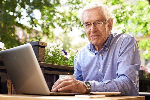Portrait of smiling senior man working with laptop in outdoor cafe lounge, 