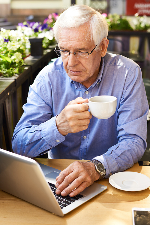 Portrait of senior man using laptop computer enjoying coffee break in outdoor cafe lounge