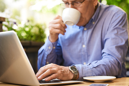 Closeup image of senior man using laptop computer enjoying coffee break in outdoor cafe lounge