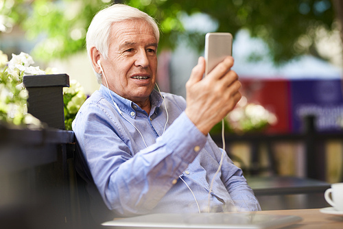 Portrait of  handsome senior man using video chat by smartphone in outdoor cafe