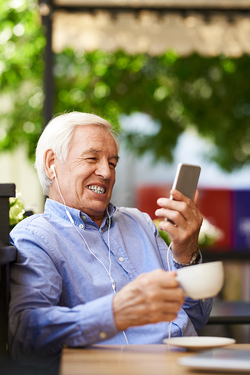 Portrait of happy senior man using video chat by smartphone in outdoor cafe, enjoying coffee break
