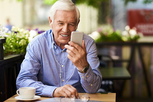 Portrait of happy senior man using video chat via smartphone in outdoor cafe, enjoying coffee break