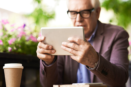 Portrait of senior man using digital tablet in outdoor cafe, focus on male hands holding modern device