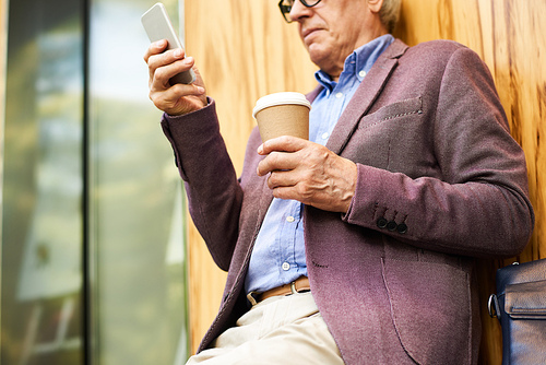 Closeup of contemporary senior man using modern smartphone outdoors