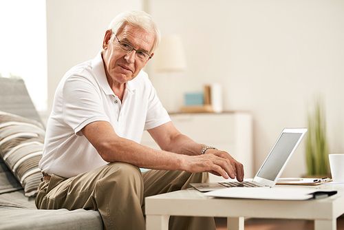 Portrait of modern senior man using laptop at home and smiling