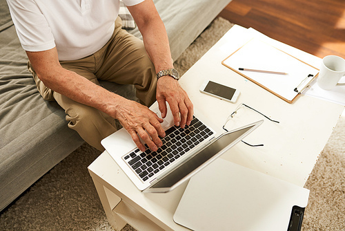 Above view of senior businessman using laptop at home, closeup of male hands typing on keyboard while working